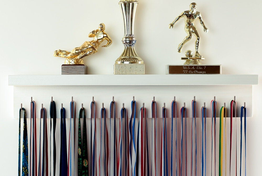 Three gold trophies displayed above a row of hanging medal ribbons.